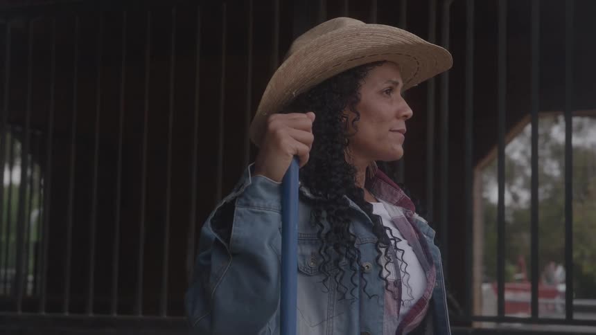 Woman with a hat holding a tool in front of a stable