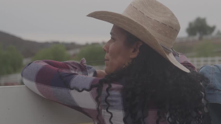 The woman is leaning on the fence of the ranch