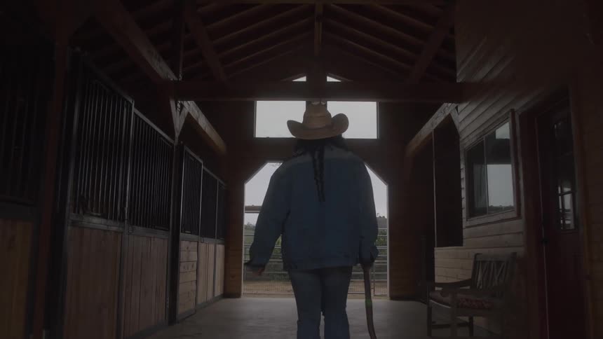 The woman walks through the barn dragging a shovel