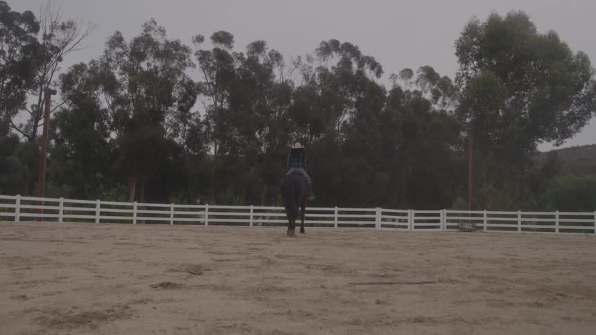 A woman riding a horse away from the camera in a fenced area