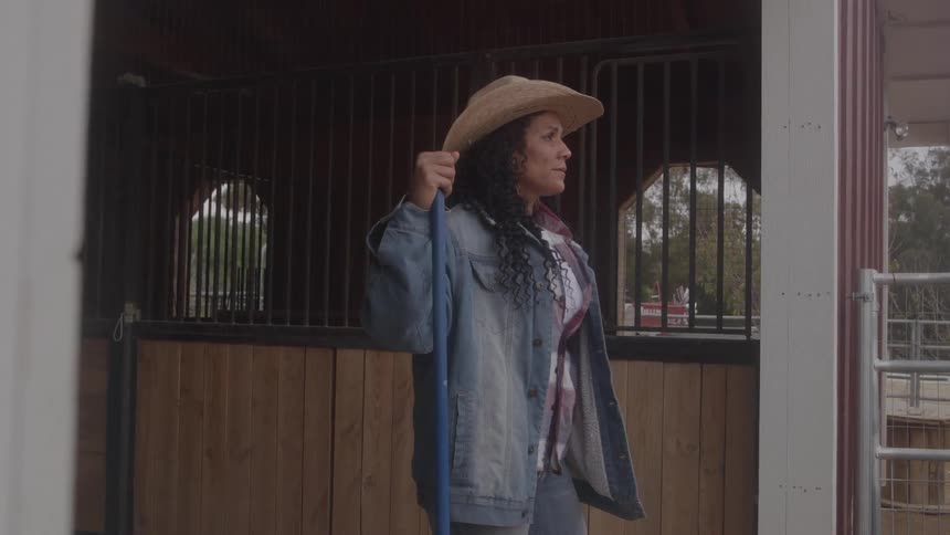 A person stands in a barn and holds a long pole
