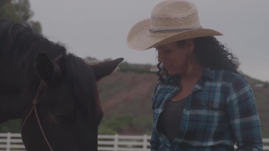 Woman with a hat closely observing a horse in the enclosure