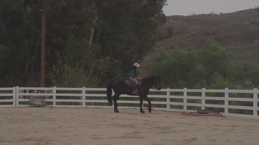 A young woman riding a horse outdoors in a paddock during daytime