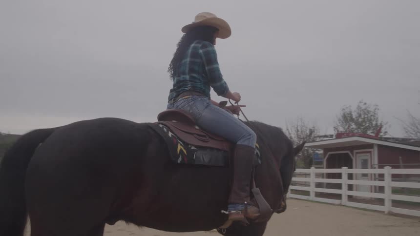 A young woman riding a dark brown horse in an outdoor paddock during daytime