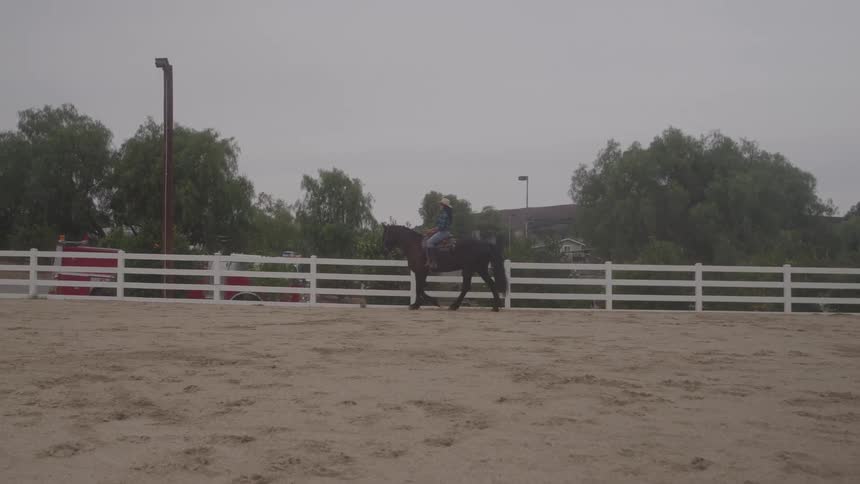 The woman is horseback riding on the ranch
