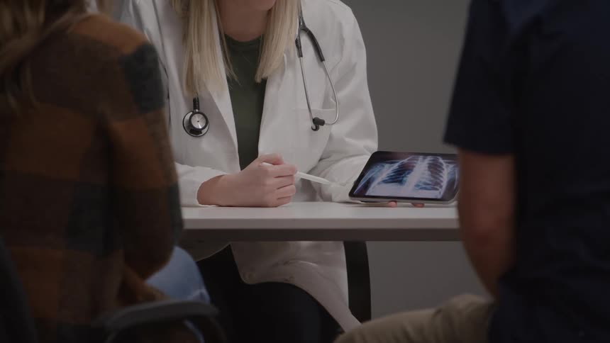 Healthcare professional reviews chest xray on tablet during consultation with three people seated around the table