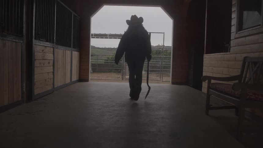 A cowgirl walks through a barn
