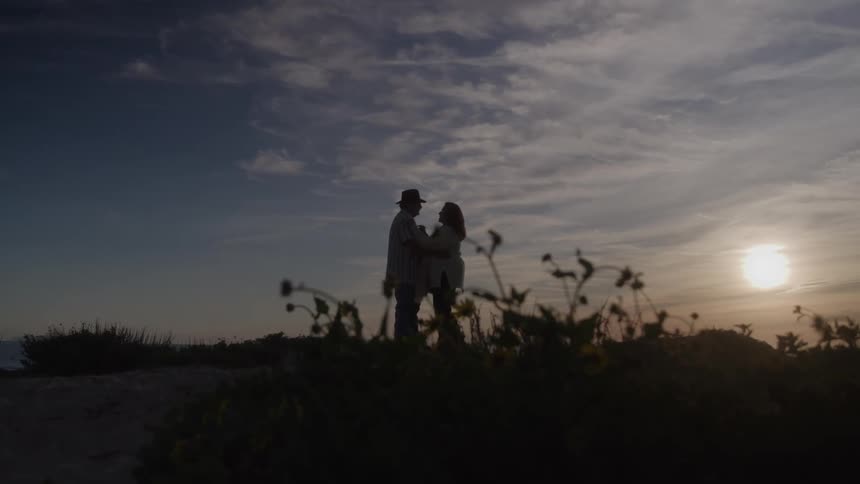 A man and woman embrace in front of the sunset