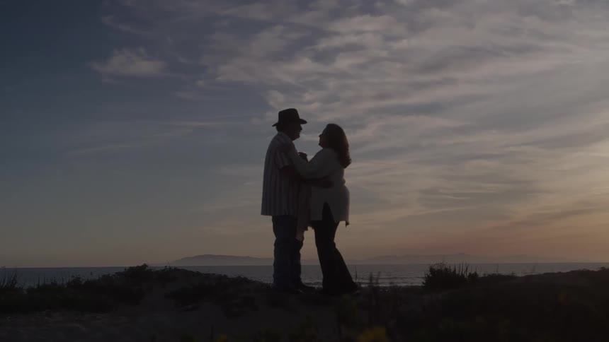 Couple faces each other holding hands by the sea at sunset