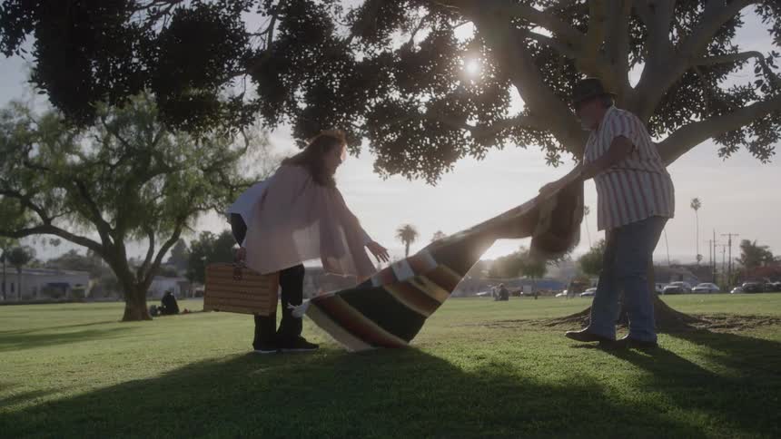Couple lays out a blanket on the grass for a picnic at sunset