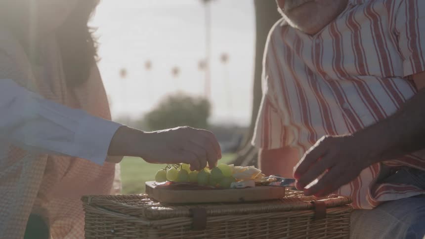 Two hands reach for fresh fruits on a picnic basket
