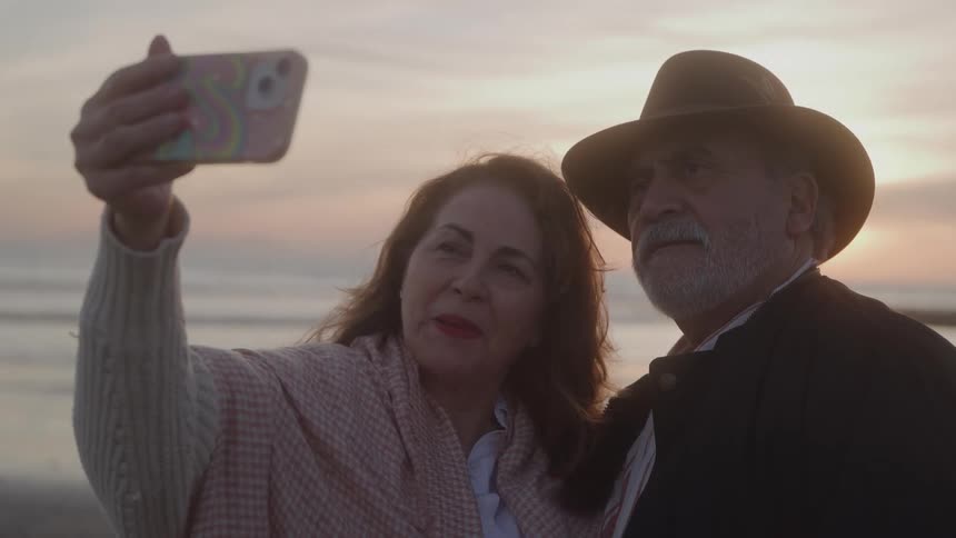 A couple takes a selfie together on a beach at sunset