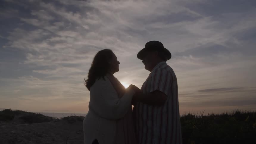 A couple holding hands standing and staring into each others eyes on the beach at sunset