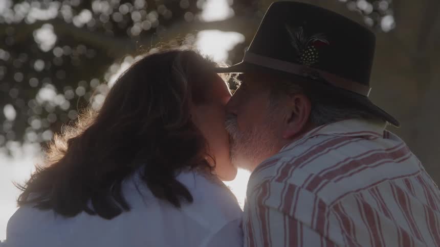 Couple kisses outdoors with sunlight in the background