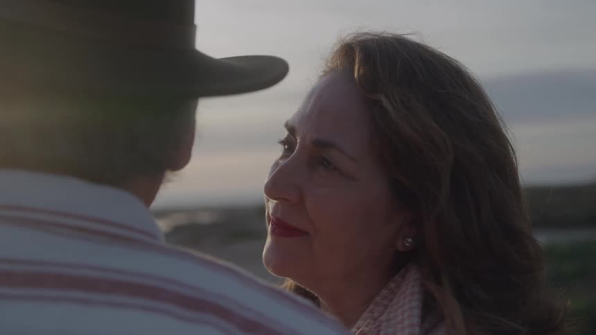 Brownhaired woman looks affectionately at a man wearing a hat