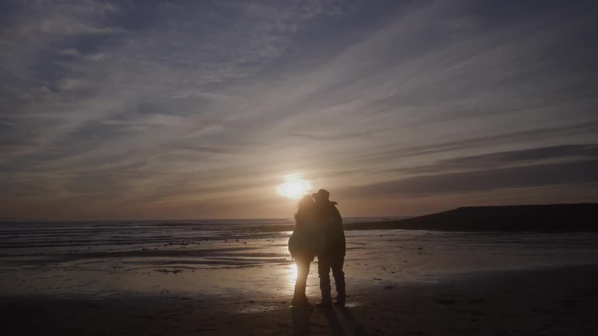 A couple embraces on a sandy beach at sunset