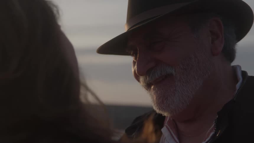 Man wearing a hat smiles while looking at the woman in front of him