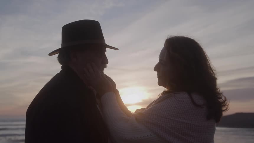 Couple looks at each other lovingly by the sea at sunset