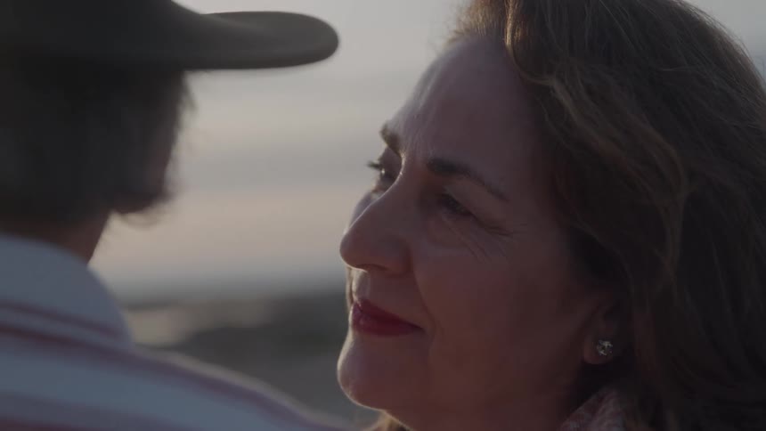 Brownhaired woman smiles while looking at a person wearing a hat in front of her