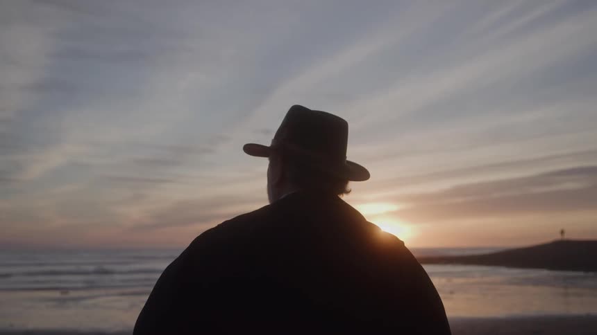 Man with a hat watches the sunset by the sea