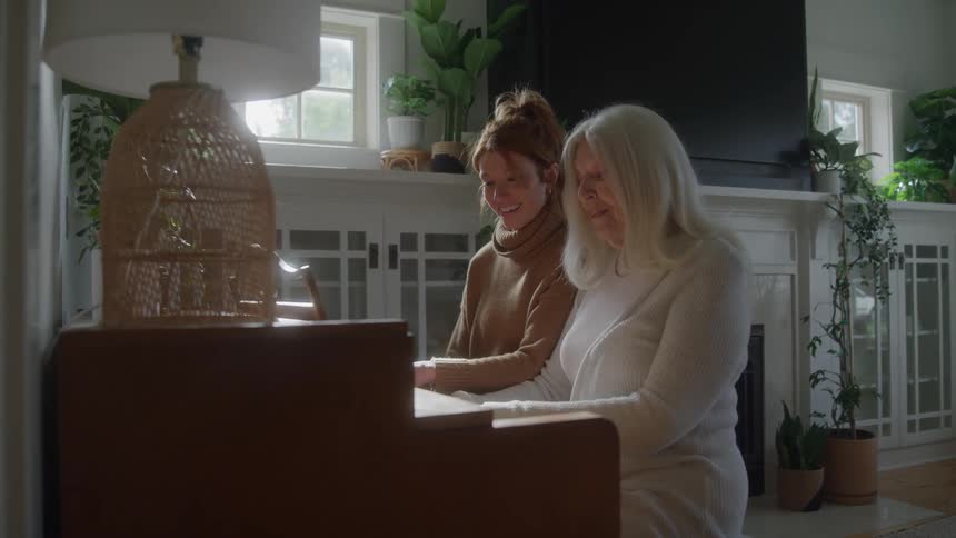 Young woman and elderly woman play piano together in a bright living room