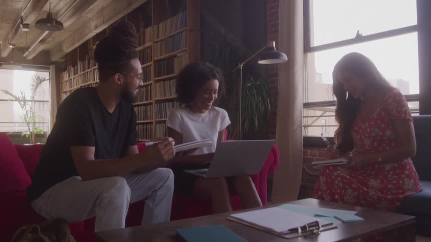 Three people sit in a room with books while collaborating