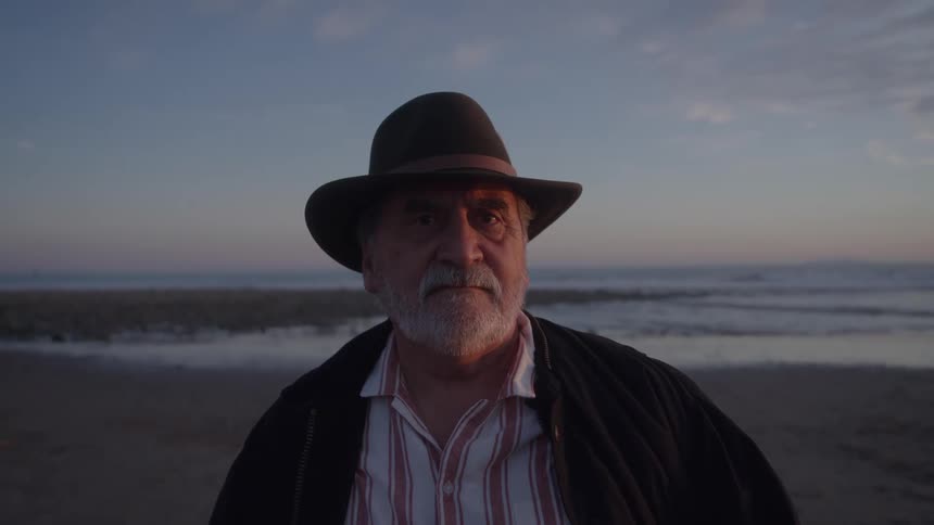 Man wearing a hat poses on the beach at dusk