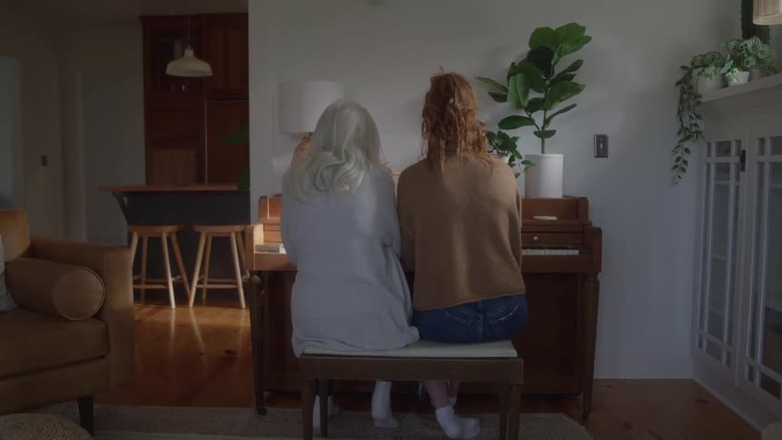 Two women sitting at the piano in a bright room