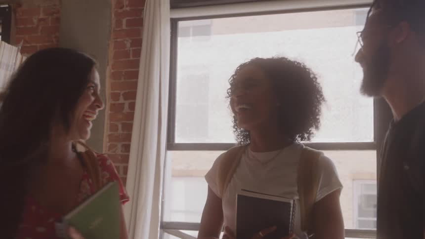 Three friends standing and having a fun conversation in a library