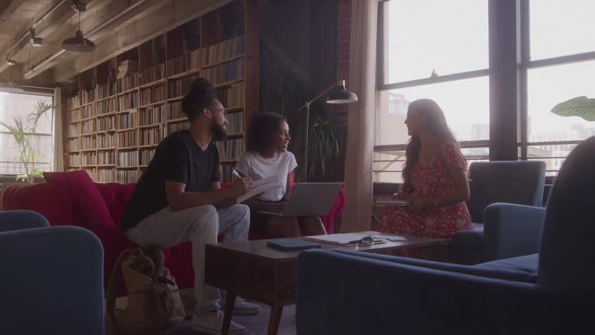 Three people talking in a room with a bookshelf