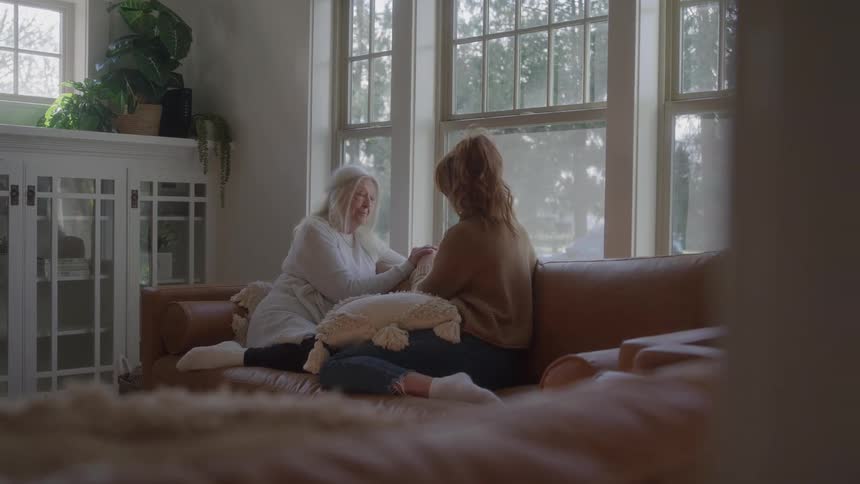 Two womenone elderly one youngsitting on a couch discussing at midday