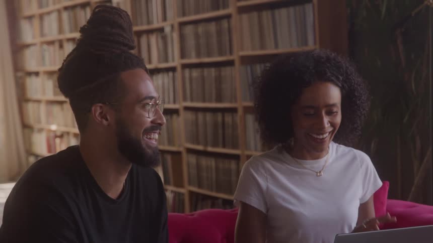 Man and woman sitting on a red couch smiling while looking at a laptop