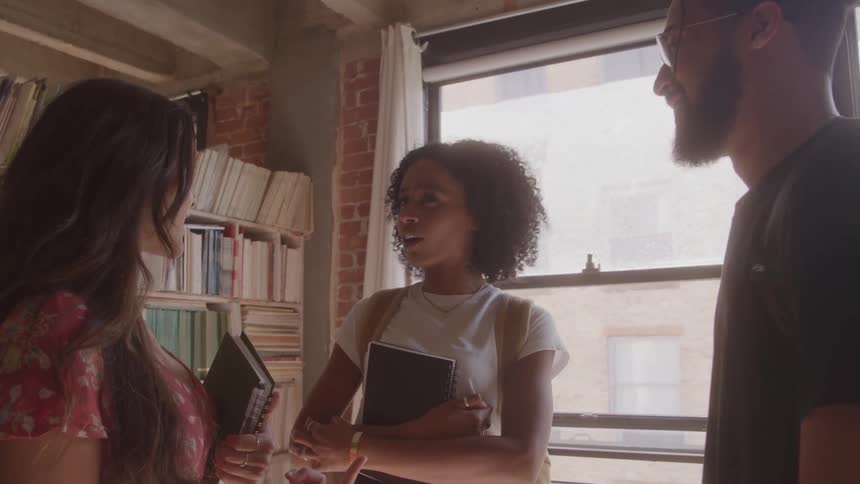 Three people chat in a naturally lit room while holding notebooks