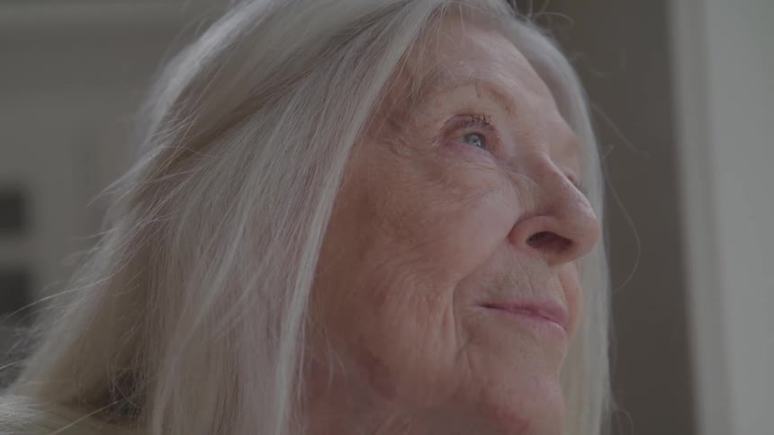 An elderly woman face is shown in a closeup from the side in an indoor setting
