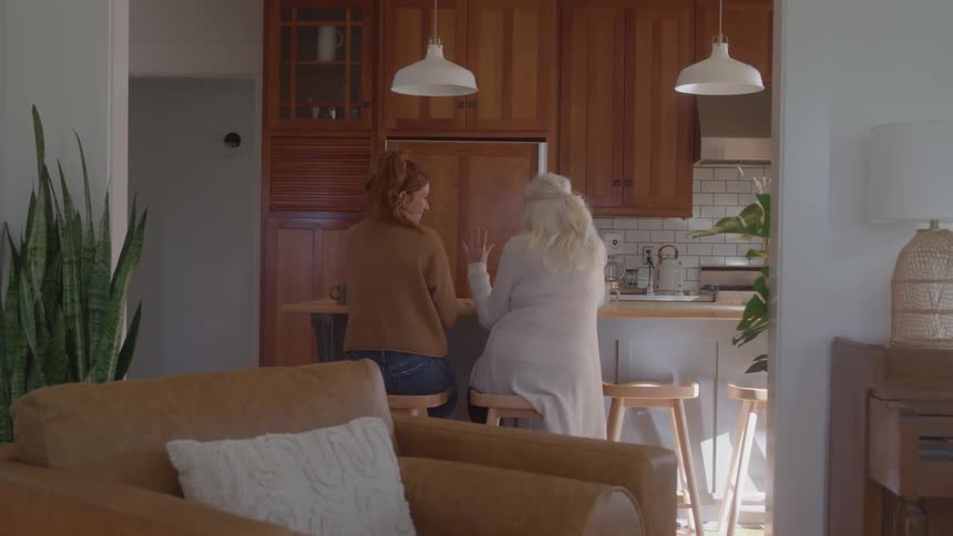 Two women sitting on stools talking in the kitchen