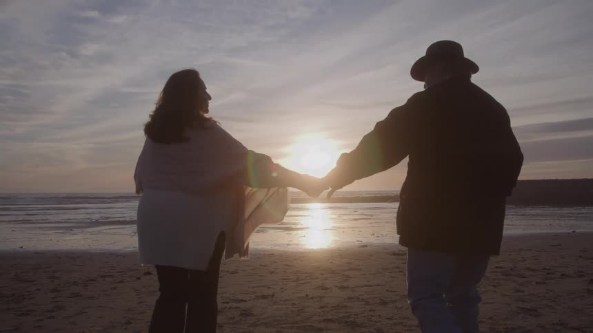Couple holding hands walking on the beach at sunset