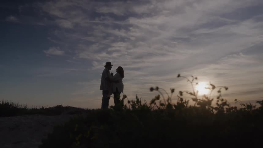 Couple stands side by side watching the horizon during sunset in natural landscape with dramatic sky and surrounding vegetation