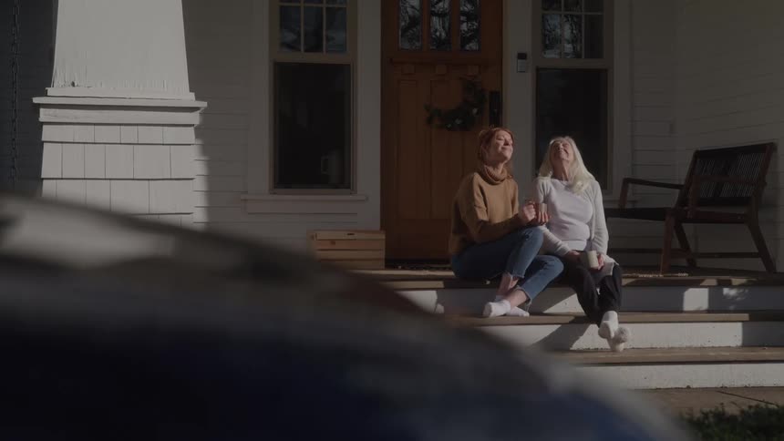Two women relax on the porch steps enjoying the sunlight