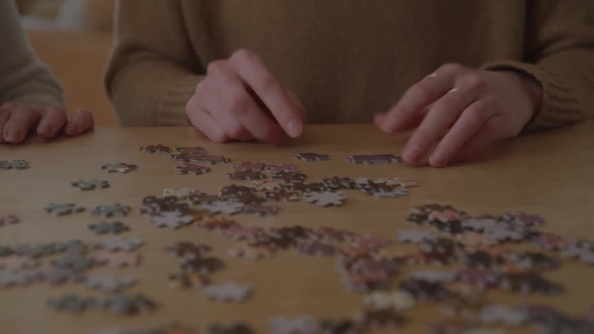 Two people sit at a table and use their hands to move puzzle pieces