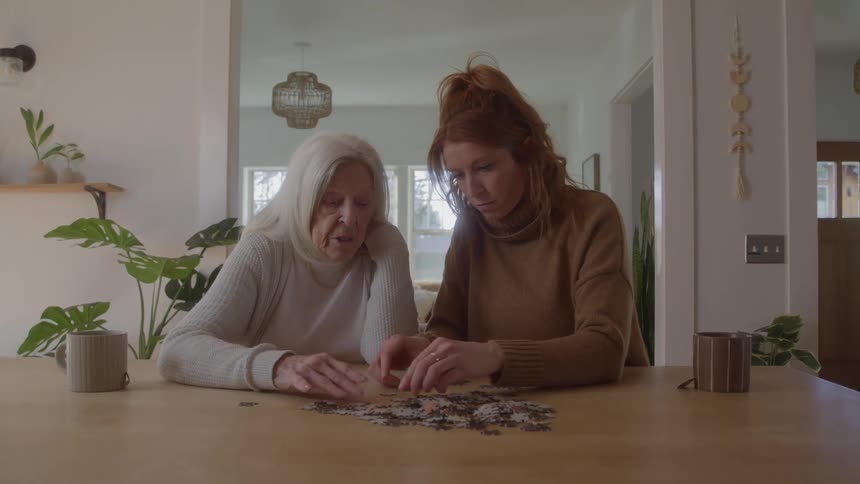 Grandmother and granddaughter sorting a puzzle on dining table