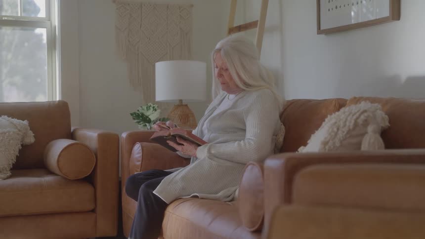 Elderly woman sitting on the sofa reading a bible