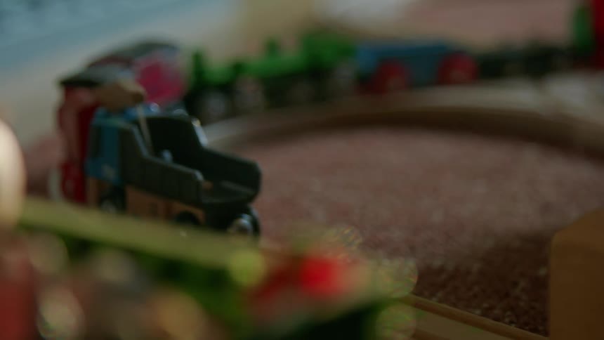 A persons hand pushes a toy train on a track and the train moves across the track