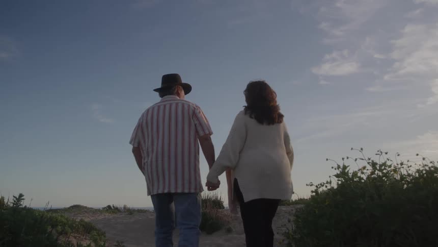 Couple walking hand in hand along a trail surrounded by vegetation