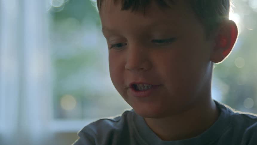 A boys face is shown he looks at the camera then looks down and smiles