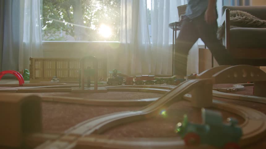 Boy playing with a wooden train track on the living room carpet
