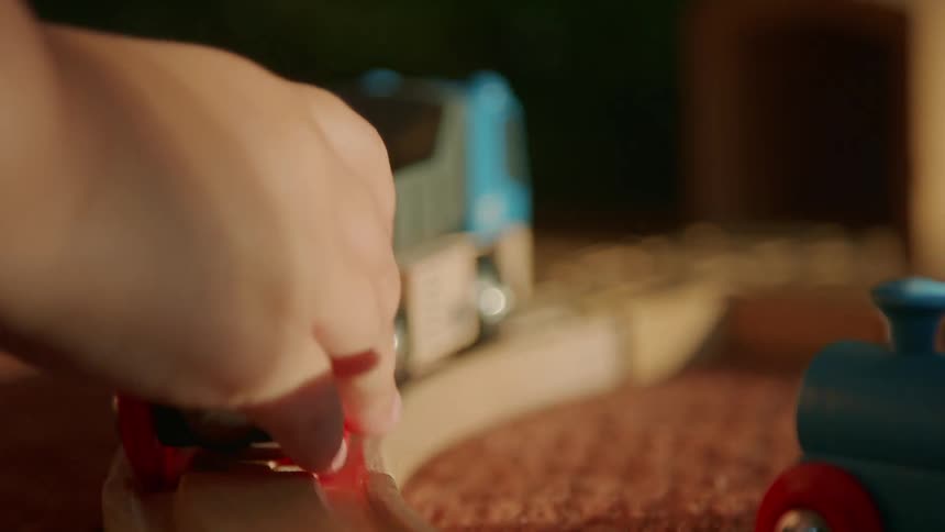 A persons hand moves a toy train along a track and out of the shot