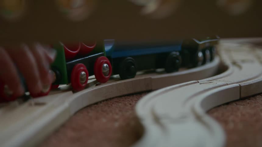 The person pushes the toy train on the tracks