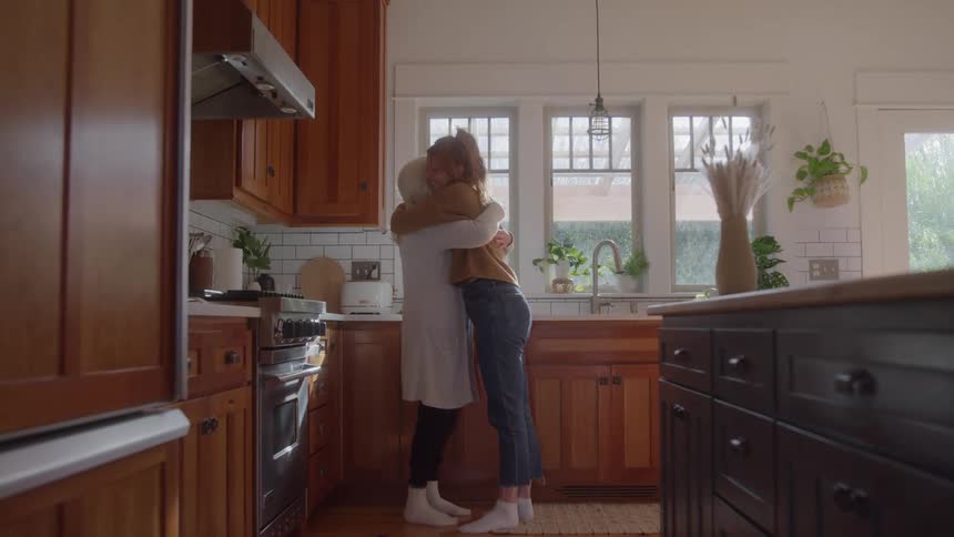 Two women embrace affectionately in the middle of the kitchen