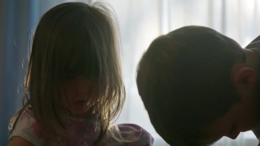 Two children play together in a softly lit room with sunlight streaming through the window
