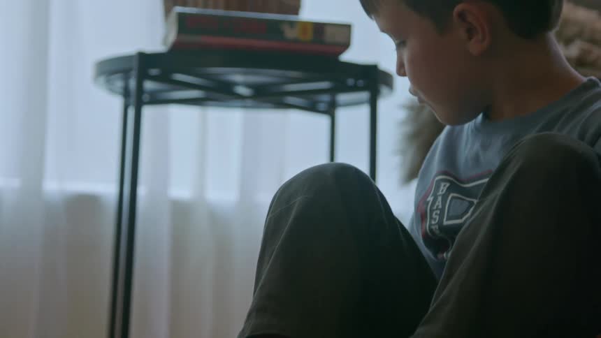 A young boys hands move a toy train on a track the boy then sits and looks at the toy another person is also on the floor